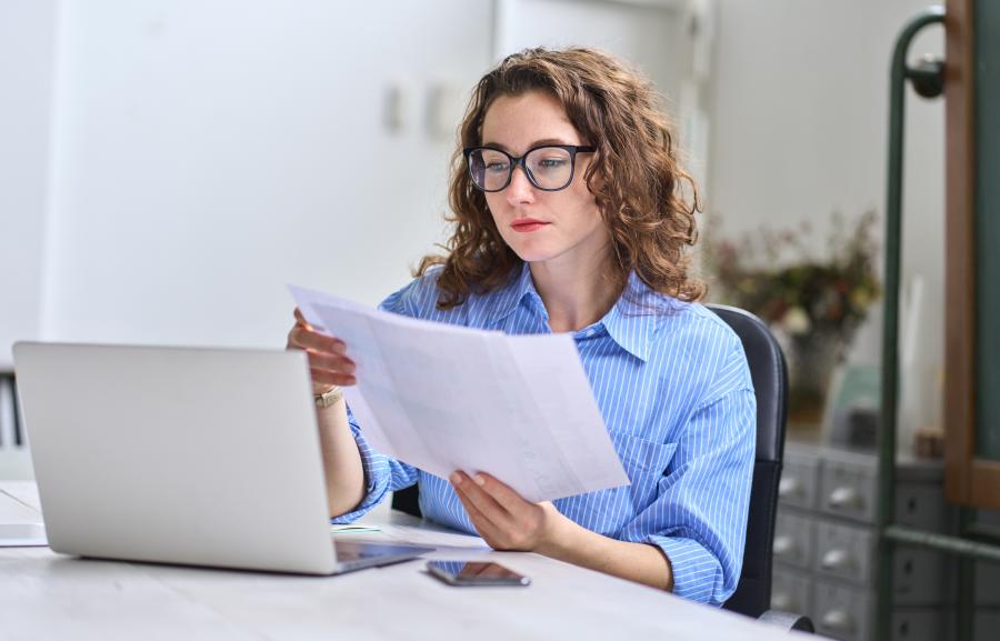 Female worker sat at desk using laptop and paper, in a domestic environment